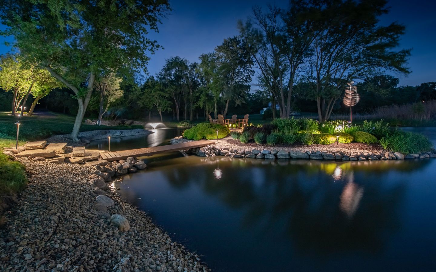 A pond with a bridge and trees at night

Description automatically generated